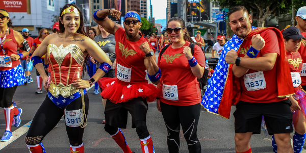 A group of four male and female racers pose for a photo with their best super hero pose. They are wearing Wonder Woman clothing and accessories.